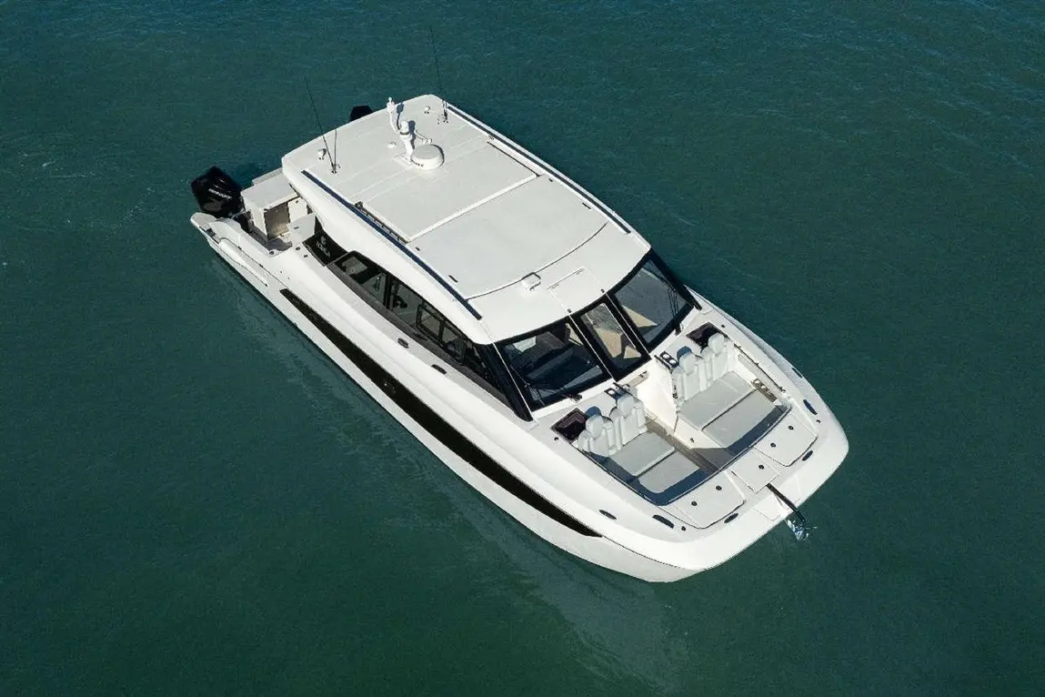 Aerial view of a sleek white motorboat with spacious seating, positioned on clear blue water, showcasing modern design and features.